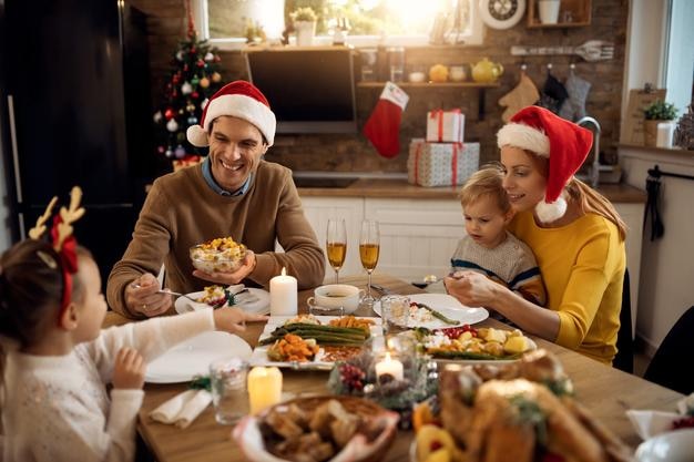 家でクリスマスを祝いながら昼食をとっている幸せな親とその子供たち