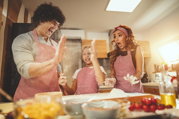 Photo happy parents and their daughter are having fun and preparing dough for pizza together in the kitchen. little girl helps to her parents to mix dough on the table.