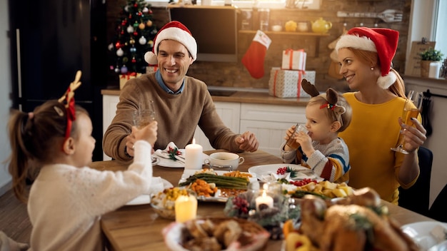 Genitori felici e bambini che si divertono mentre brindano durante il pranzo di natale nella sala da pranzo