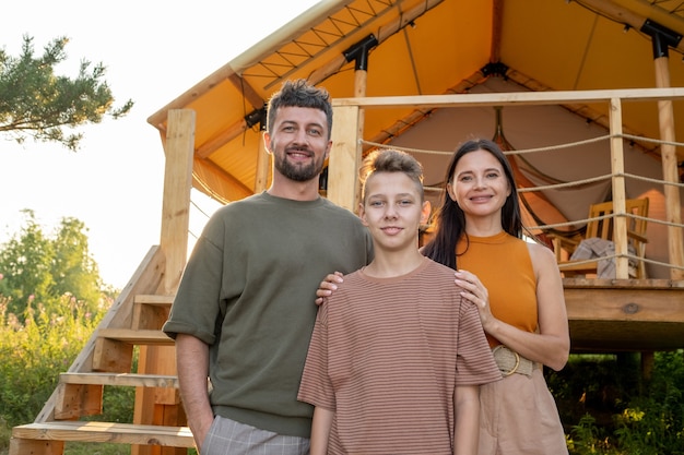 Photo happy parents and their teenage son standing by glamping house