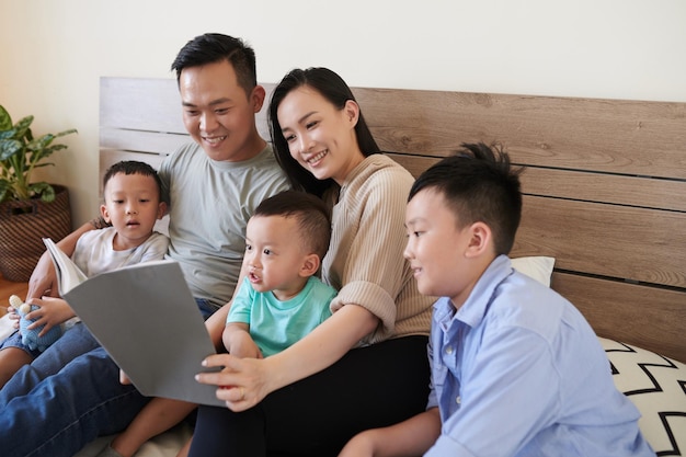 Happy parents and three children sitting on bed and reading new book together