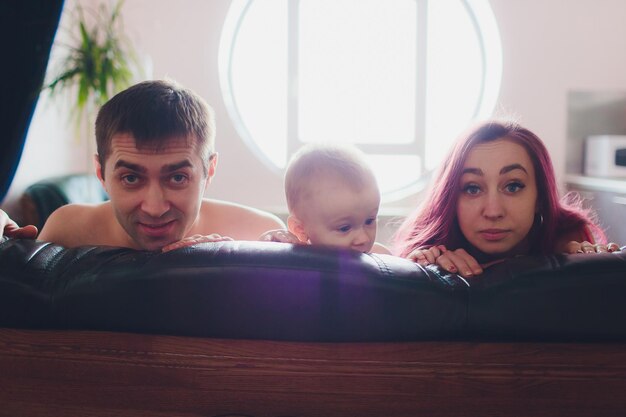 Photo happy parents with adorable little baby girl sitting on the couch at home enjoying parenthood young happy family new life concept