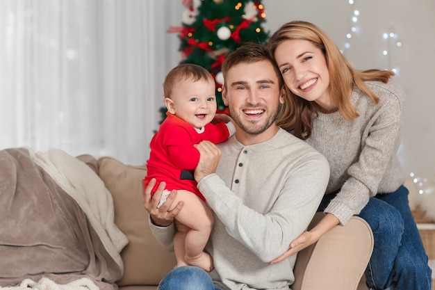 Happy parents with baby in decorated room for Christmas