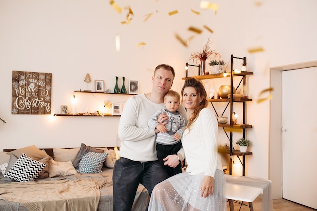 Happy parents with little cute child standing together in wonderful studio, hugging, looking at front and posing