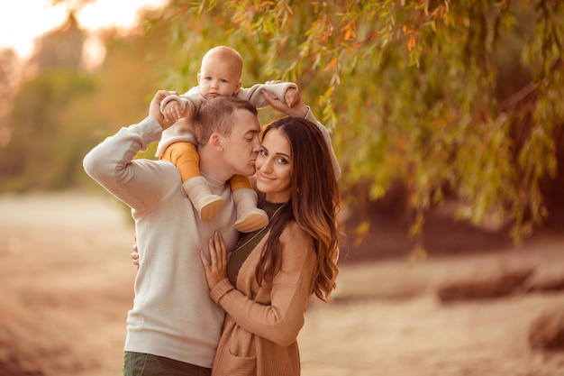 Happy parents with a small child on their shoulders for a walk in the autumn in the park