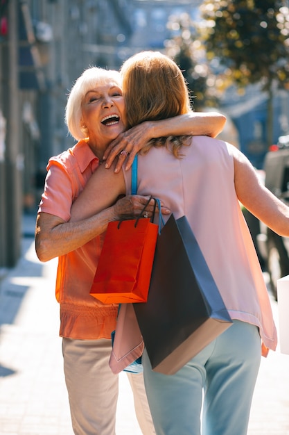 通りで彼女の娘を抱き締める紙袋を持つ幸せな年金受給者