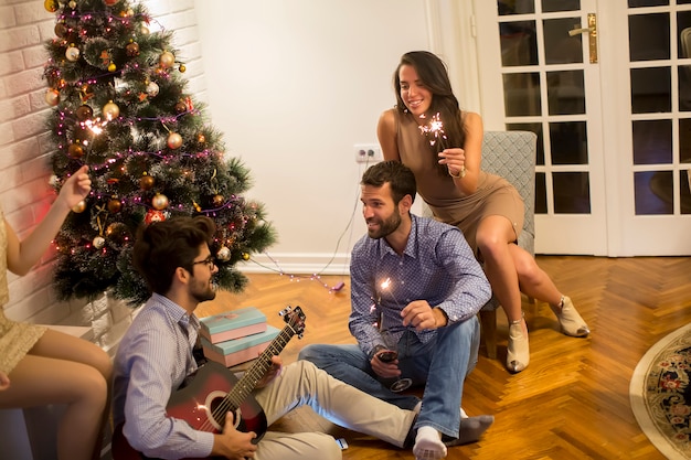 Gente felice che celebra il natale e il nuovo anno con l'abete a casa e suonando la chitarra