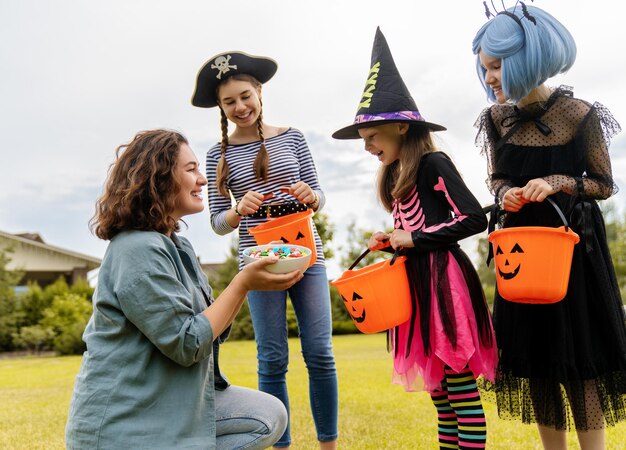 Photo happy people celebrating halloween adult is treating with sweets children outdoors