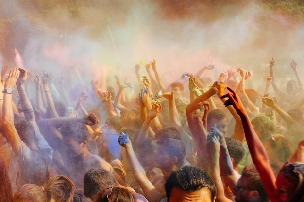 Happy people crowd partying under colorful powder cloud at holi fest festival of colors in summer amazing moment