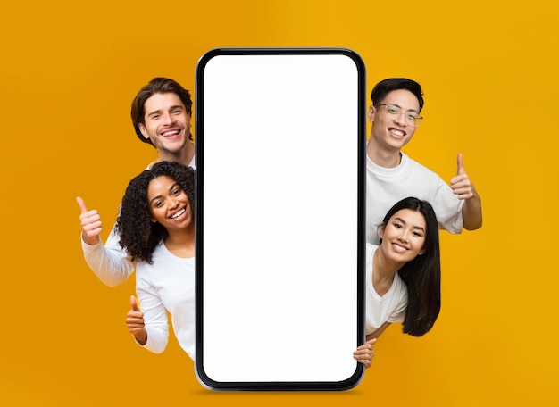 Happy People Peeking Out Behind Big Blank Smartphone And Showing Thumb Up