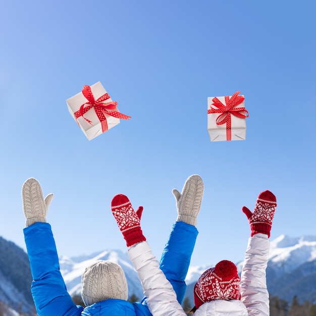 幸せな人々は青い空と雪の山々の背景にクリスマスギフトボックスを投げます