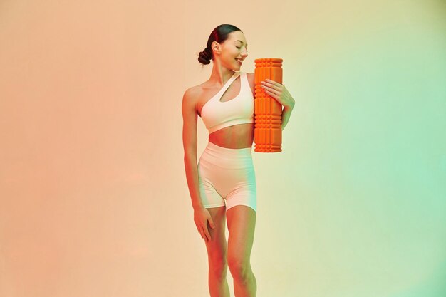 Happy person holding roller Young fitness woman in sportive clothes against background in studio