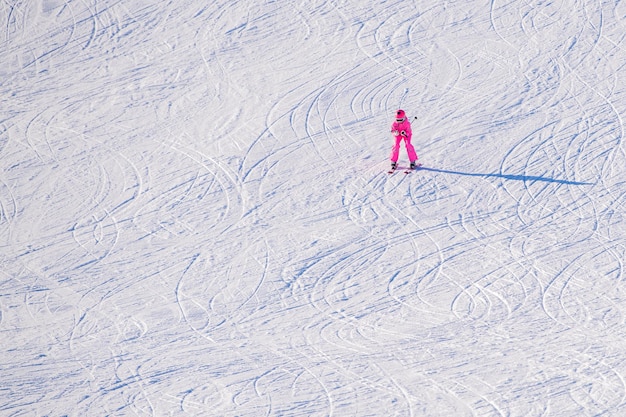 赤いジャケットを着た幸せな人が、青空に明るい日差しの中で坂を下ってスキーをし、高雪に覆われた山々を背景にぼやけた動き