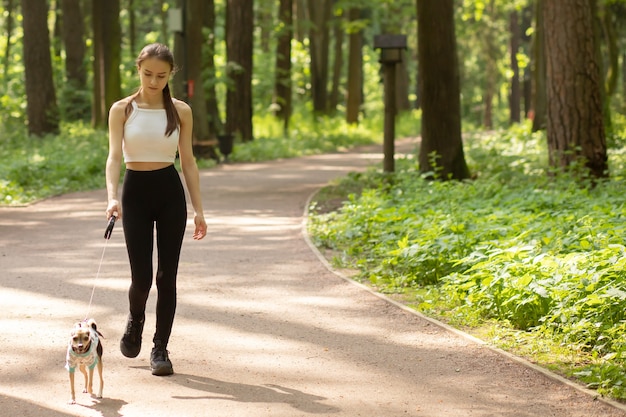 幸せなペット。若い女の子が公園で小さな犬と一緒に歩く