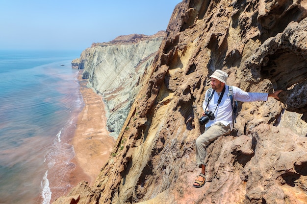 崖の端、ホルムズ島、ホルモズガーン、イランに座っている幸せな写真家の旅行者。