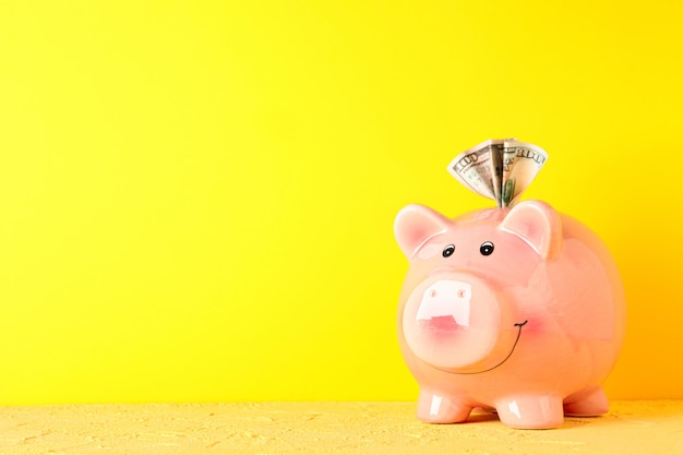 Happy piggy bank with dollar on yellow table against color background