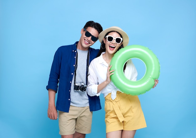 Happy playful Asian couple tourist dressed in summer clothes and beach accessories to travel on holidays on blue.