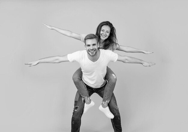 Happy playful woman and man pretend flying doing piggyback ride yellow background fun