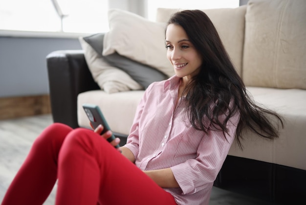 Happy pleasant woman resting at home holding smartphone smiling young lady chatting on social networks watching funny videos and using mobile apps at home