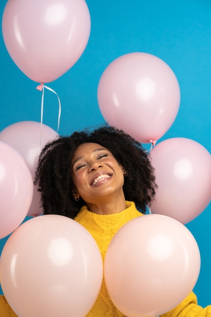 ピンクの風船をたくさん持っている幸せな幸せなアフリカの女性は、誕生日を祝うクールなパーティーを楽しんでいます