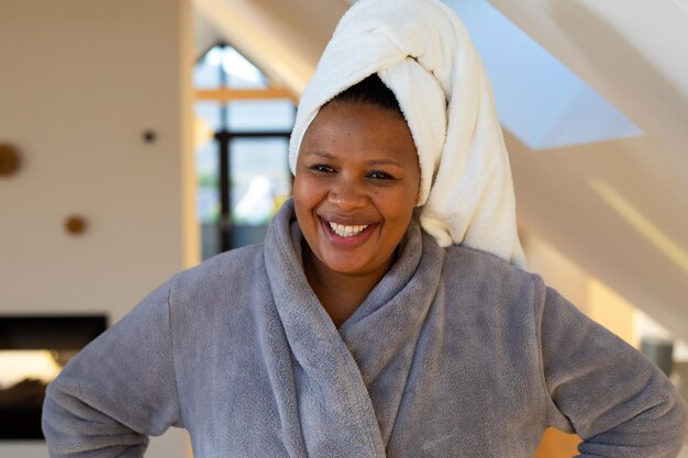 Foto felice donna afroamericana di taglia plus che indossa un accappatoio, sorridente in bagno.