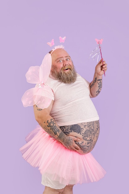 Happy plus size male person in fairy costume poses on purple background