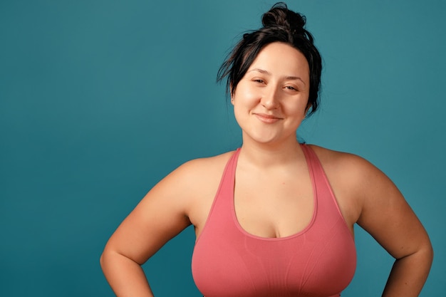 Happy plus size positive woman. Happy body positive concept. I love my body. Attractive overweight woman posing on camera in the studio on a colored background. Girl is wearing a coral bra