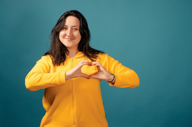 Happy plus size positive woman. Happy body positive concept. I love my body. Attractive overweight woman posing on camera in the studio and make heart from her fingers.