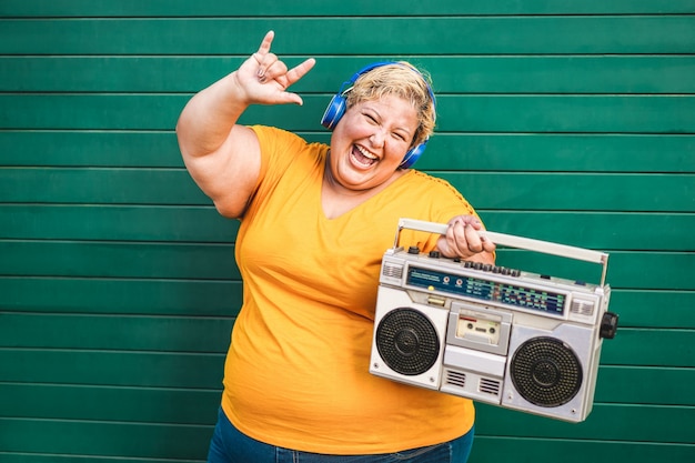 Happy plus-size woman dancing and listening to rock music with vintage boombox