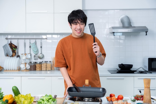 幸せなアジア人の若い男の肖像画 楽しい料理を準備し,料理を楽しむ