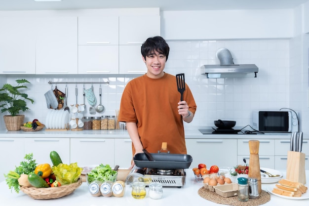 アジアの若い男の幸せな肖像画 喜びに満ちた食事の準備をして 料理を楽しむ 野菜で料理を料理しながら キッチンに立っている コンドー生活や家