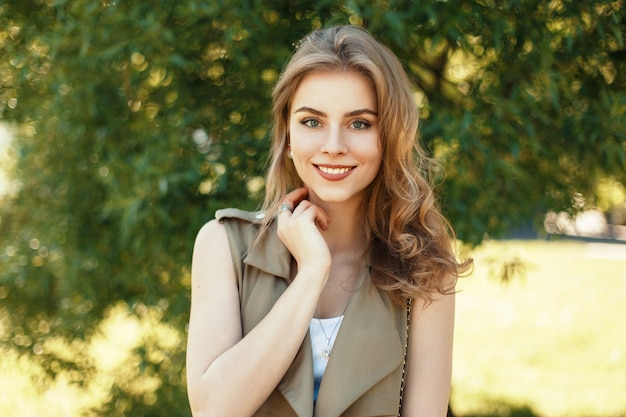 Happy portrait of a beautiful cheerful woman with a sweet smile near a tree on a spring sunny day