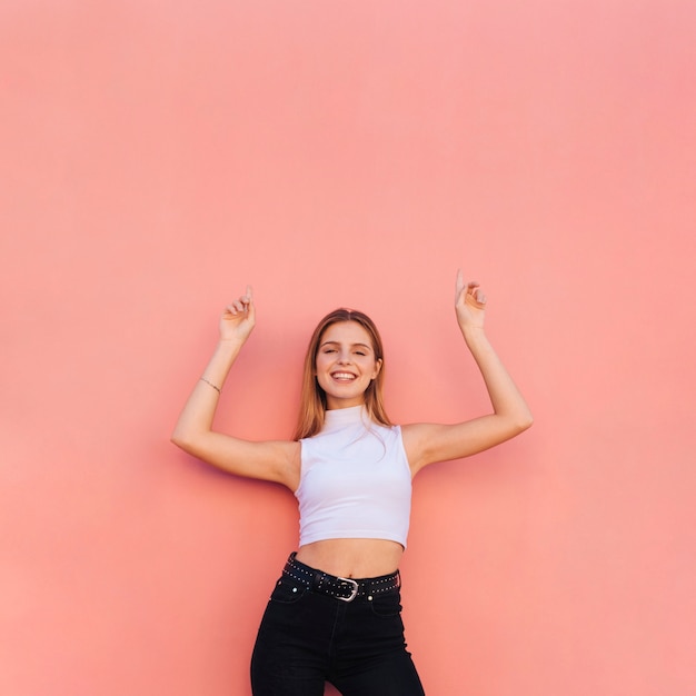 Happy portrait of a beautiful young woman raising her arms pointing fingers upward