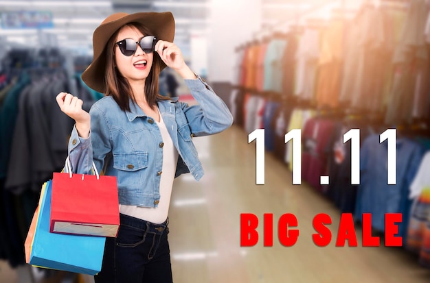 Photo happy portrait beautiful young woman smiling with sunglasses and hat she excited holding shopping bags multi color on the mall with 11.11 big sale text on space, 11:11 shopping sale concept