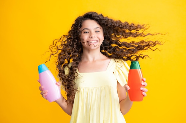 Happy portrait of child teen girl with shampoos conditioners and shower gel Long hair care of teenager Presenting cosmetic product shampoo bottle Smiling girl