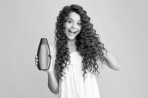 Happy portrait of child teen girl with shampoos conditioners and shower gel Long hair care of teenager Presenting cosmetic product shampoo bottle Smiling girl