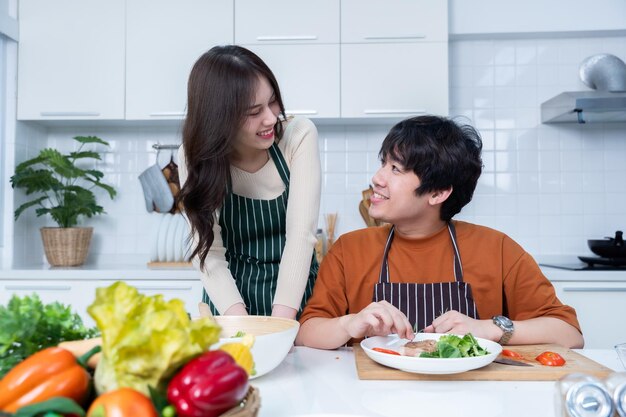 Photo happy portrait of loving young asian of having fun standing a cheerful preparing food and enjoy cook cooking with vegetables meat bread while standing on a kitchen condo life or home