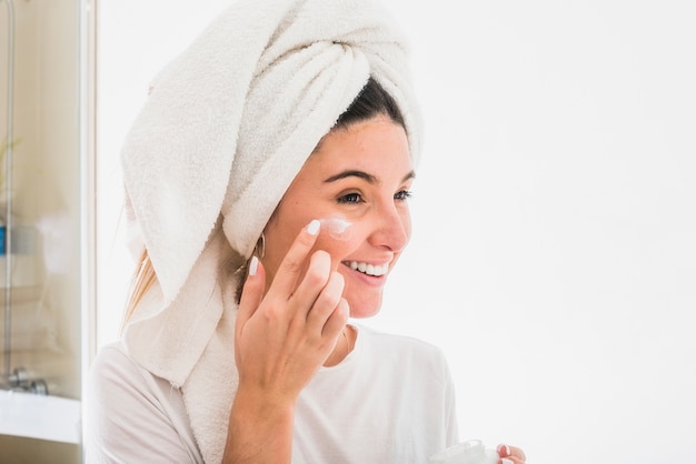Ritratto felice di una giovane donna che applica la crema sul viso