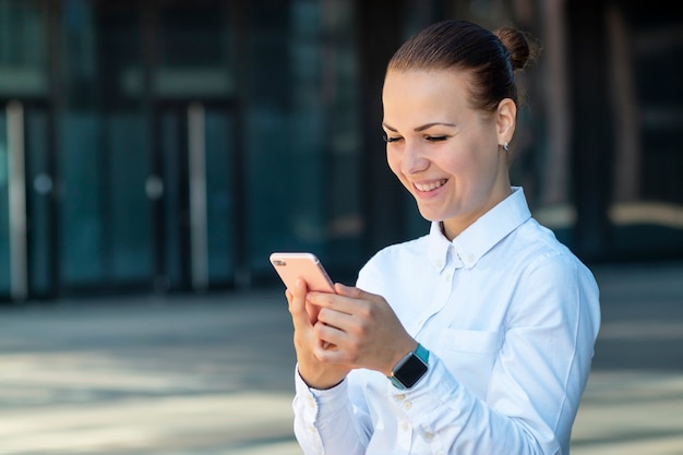 Happy positive cheerful business woman, young beautiful girl looking at smartphone