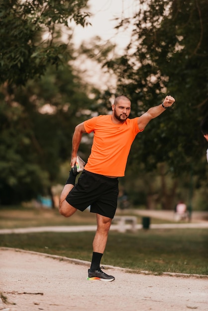 야외 운동 중 행복한 긍정적인 스포츠맨은 운동복을 입고 공원 밖에서 활동적인 생활 방식을 즐기는 근육을 워밍업합니다.