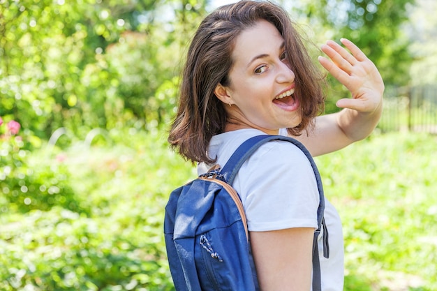 Happy positive student girl with backpack smiling on green park background.