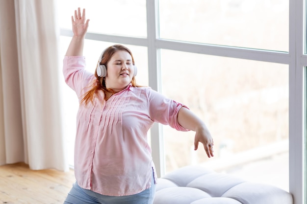 Happy positive woman dancing to her favourite music while being in a perfect mood