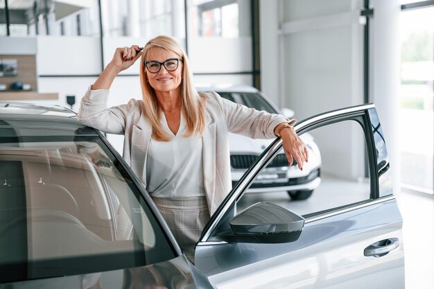 Foto felice donna positiva in abiti formali bianchi è nel concessionario auto