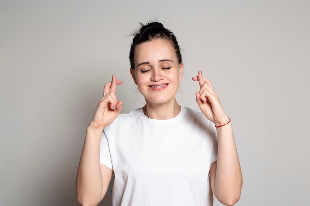 A happy positive young woman with crossed fingers makes a wish closes her eyes