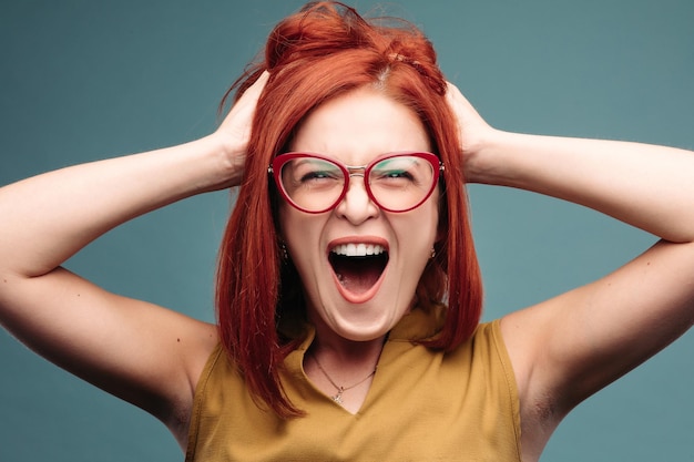 Happy and positivity red haired woman in eyeglasses shouting holding head by hands