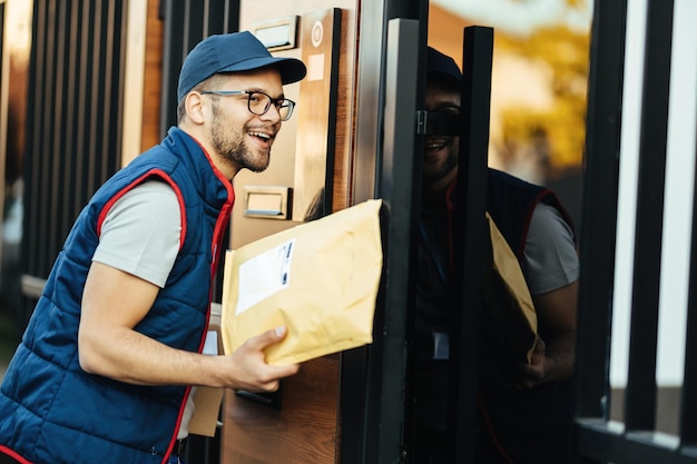 Happy postal worker delivering package to his customer and ringing on intercom at front gate