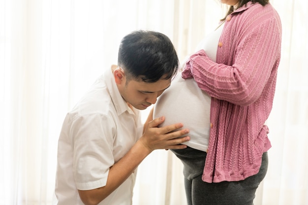 Happy pregnant couple of husband and wife. Young expecting woman holds baby in pregnant belly.