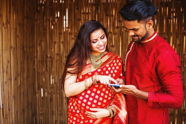 Happy pregnant Indian woman with her husband using phone