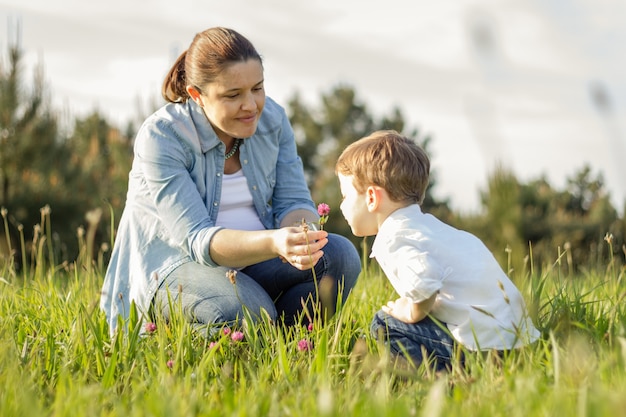 Happy pregnant mother and cute son picking a bouquet of flowers in a sunny field