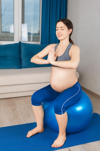 행복한 임신 한 여성은 집에서 운동을합니다. 임신 한 어머니는 적합한 공을 명상합니다. 임산부 요가 건강한 생활 방식 개념